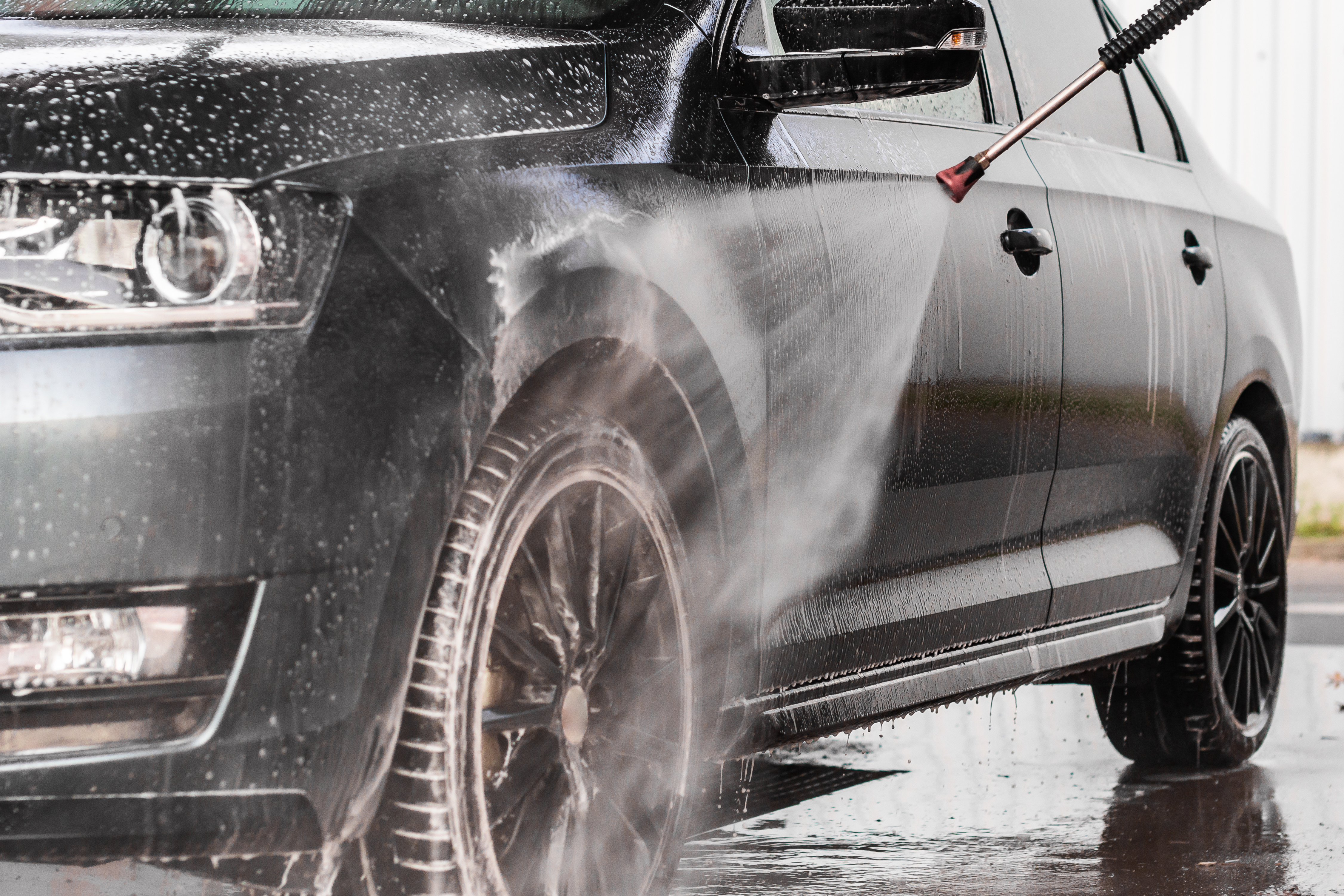 A man is washing a car at self service car wash. High pressure vehicle washer machine sprays foam.